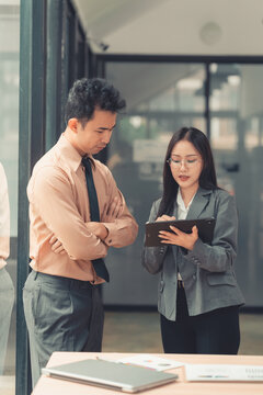 Two Asian business colleagues discussing work project on digital tablet in office.