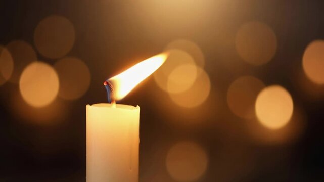 Single burning candle flame with warm golden bokeh background lights