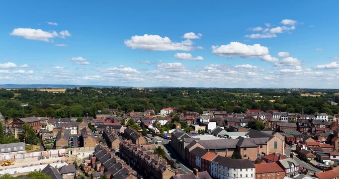 Ascending aerial drone footage over Ripon North Yorkshire England revealing the historic city centre with traditional rooftops surrounding countryside and distant landscapes beneath a blue sky