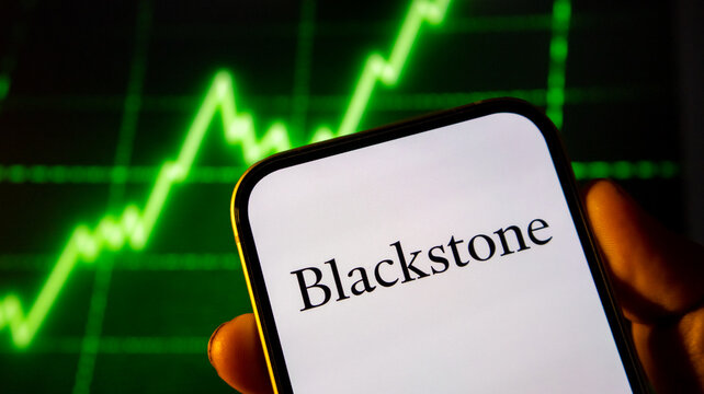 Blackstone corporate logo displayed on smartphone screen against a glowing green stock market chart background.