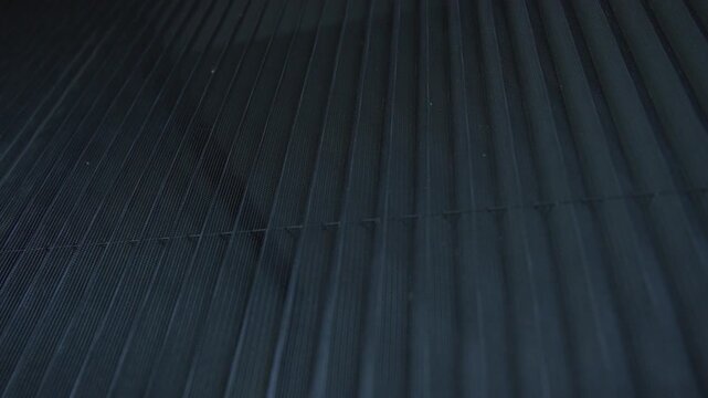 Slow motion of a pleated mosquito net on a window reveals fine vertical mesh folds in cool gray-blue tones, with subtle light passing through in a rhythmic textured pattern.