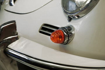 Detailed view of the front corner of a light beige classic car, highlighting its round headlight, chrome bumper and turn signal. © SKfoto GE