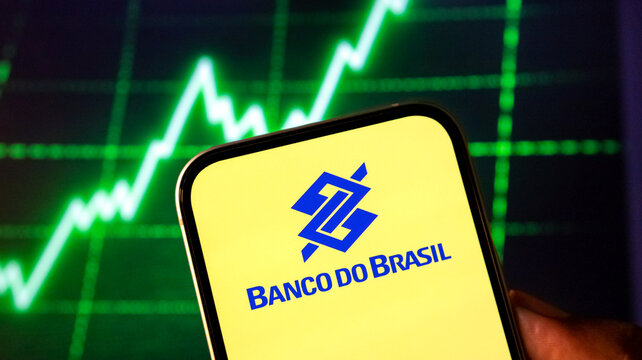 Banco do Brasil logo on smartphone screen with rising stock market chart in background.