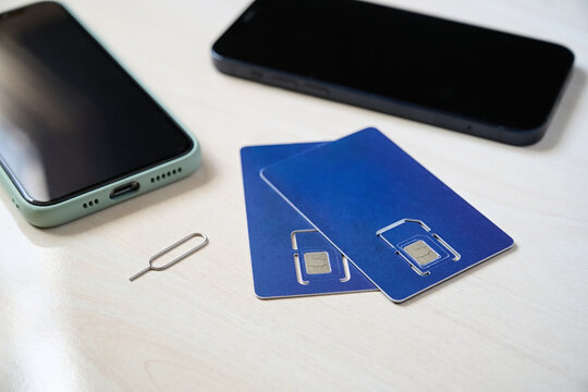 Two sim cards lying on a table, dark smartphones and paper case. Replacing SIM cards for a smartphone.