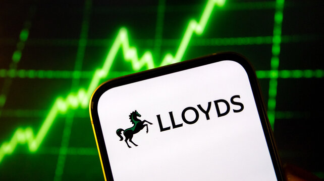 Lloyds bank logo on smartphone screen with glowing green stock market chart background showing upward trends.
