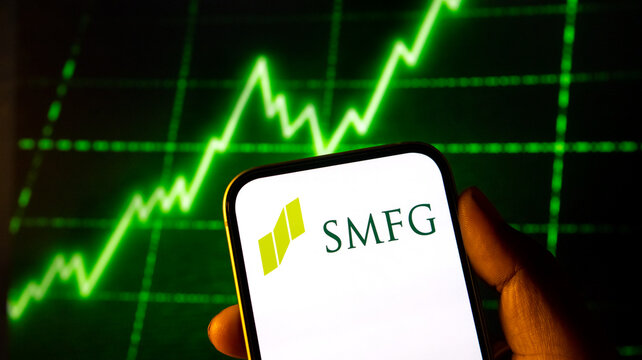 Smfg banking logo displayed on smartphone screen with green stock market growth chart on background wall.