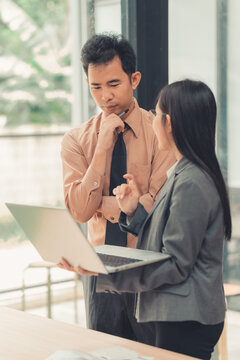 Two Asian business colleagues discussing work project on digital tablet in office.