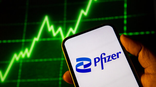 Pfizer stock market graph on smartphone screen held by hand with rising financial chart background technology.