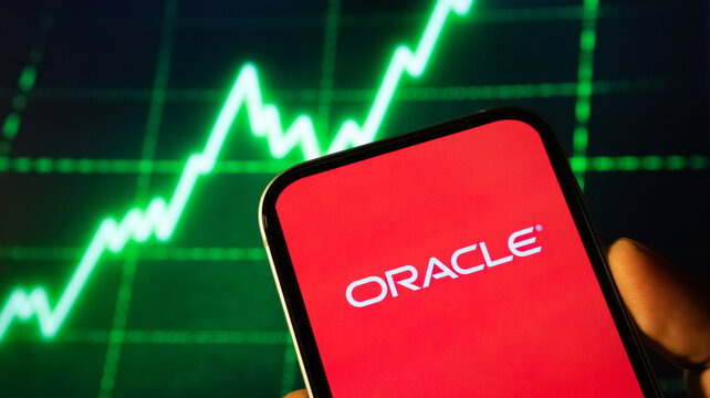 person holding smartphone with oracle logo, stock market chart displaying green uptrend in background.