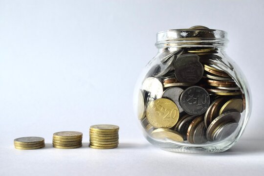 Malaysian ringgit coins stacked in an increasing order next to a clear glass jar filled with coins on a clean white background.