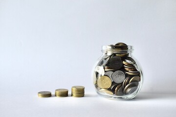 Malaysian ringgit coins stacked in an increasing order next to a clear glass jar filled with coins on a clean white background. © Akram