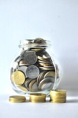 Vertical studio shot of a clear glass savings jar overflowing with diverse Malaysian coins with small stacks arranged in front, emphasizing retirement planning, financial stability, and cash savings. © Akram