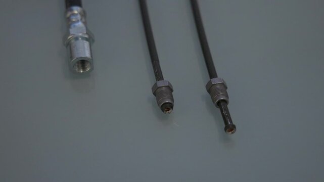 Three automotive brake lines lie on a light gray surface, showing a rubber hose with a threaded fitting on the left and two thin metal brake pipes with flare fittings on the right.