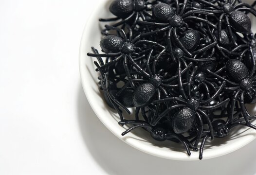 Many creepy small black plastic spiders in a white bowl for a spooky Halloween decoration