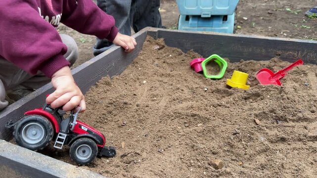 Close-up of children playing together in a sandbox with toy trucks, excavator and shovel at an outdoor playground. Creative play, imagination and early childhood development. 