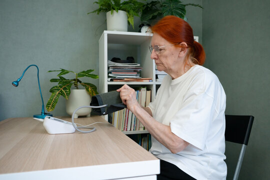 A mature woman attaches the blood pressure measurement cuff to her arm in a close-up side view. Detailed health monitoring procedure.
