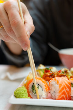 Close-up of a man hand picking up sushi with chopsticks. Skillful fingers holding a fresh salmon roll above an appetizing plate. Food photography capturing tactile dining and chopstick mastery