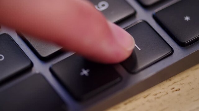 Extreme close up shot of a finger pressing the minus sign key on an external numeric keypad grid. Pushing the minus button on a 100 precent keyboard.