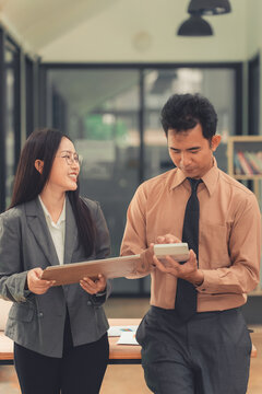 Two Asian business colleagues discussing work project on digital tablet in office.