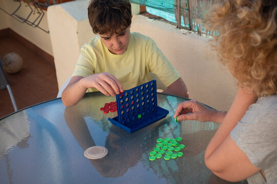 Mother and her 12-year-old son concentrating on a strategic board game during a relaxing afternoon together on an outdoor home terrace