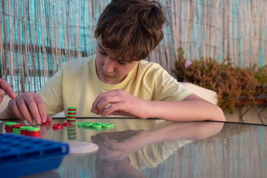 Teenager concentrating while placing game pieces during a strategy board game on an outdoor terrace at home