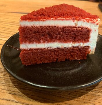 Classic red velvet cake slice with cream cheese frosting on black plate.