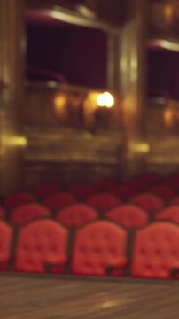 Rows of red seats are arranged in a theater. The stage is set for a performance, and the lights are dim. The atmosphere is prepared for an evening event with no audience present.