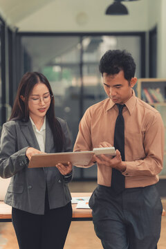 Two Asian business colleagues discussing work project on digital tablet in office.