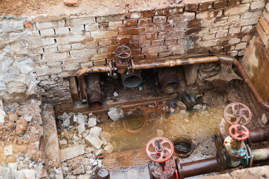 engaged in maintenance at a construction site where water pipes and valves are visible in a pit filled with water and debris