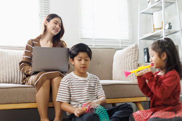 Fototapeta premium Mother multitasking, working from home on a laptop while children play cheerfully on the floor, balancing career and family life in a modern living room setting