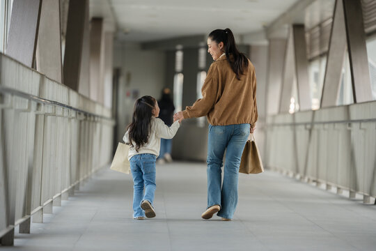 mother and child girl with shopping bag walking on footbridge in city