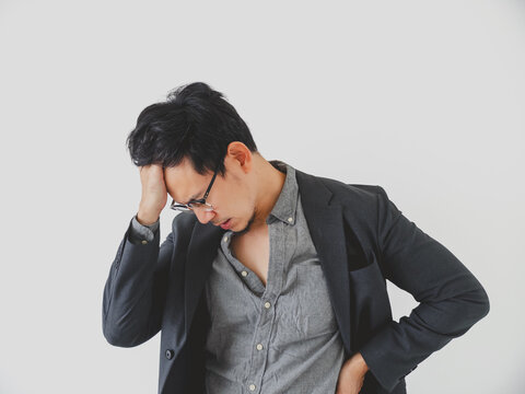 Young Asian businessman looking stressed and tired with a headache, experiencing burnout or work problems.