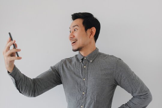 Happy Asian man smiling widely while holding a smartphone for a video call or selfie.