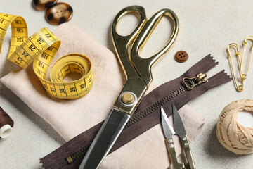 Different tailors supplies with measuring tape and beige cloth on grunge white background