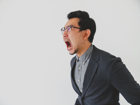 Angry Asian Businessman Screaming Loudly with Mouth Wide Open Against a Clean White Background