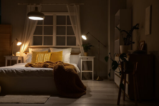 Interior of dark bedroom with window, shelf unit and glowing lamps