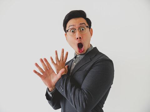 Young Asian man in suit jacket showing extreme surprise and disbelief with hands up.