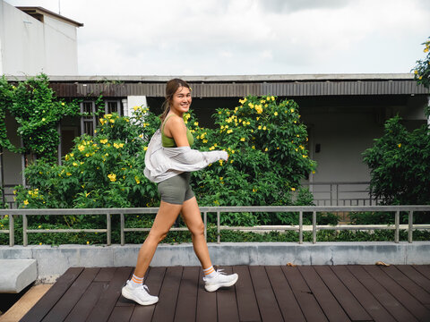 Smiling Young Asian Woman Walking Outdoors on a Wooden Deck, Embracing a Healthy Lifestyle