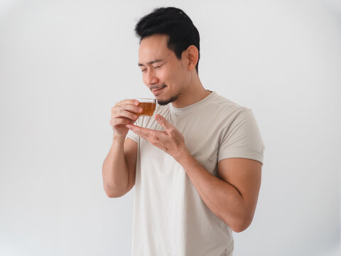 Relaxed Asian man holding a cup of tea, appreciating its soothing scent with closed eyes.