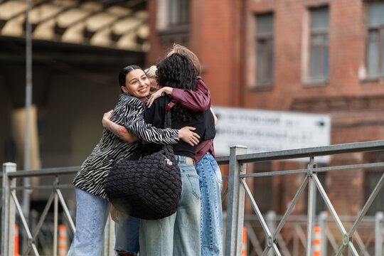 Three happy women friends in a group hug on a city street