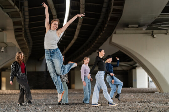 Happy young woman jumping with friends under bridge