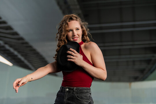 Stylish young woman with curly hair dances with a hat