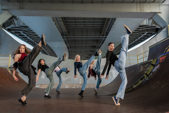 Group of young women dancing high kicks together at a skate park