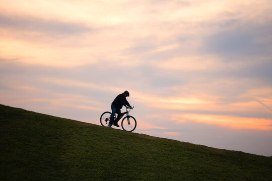 Man riding his bike up a grassy hill at sunset