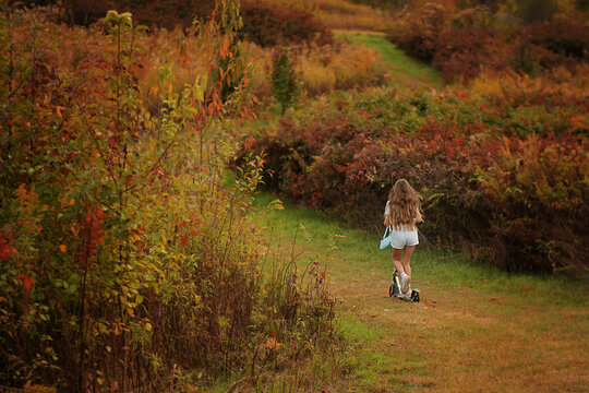 Girl rides scooter down a grassy autumn path