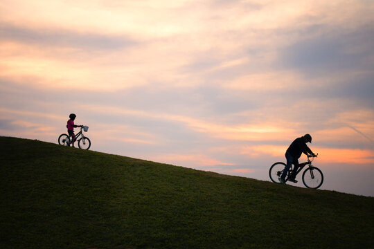 Man and child riding bikes on a grassy hill at sunset
