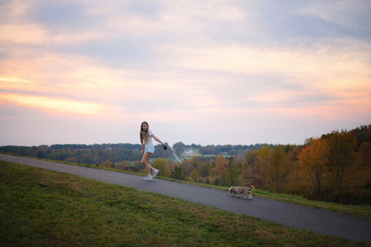 Young girl walks her Shih Tzu dog on path at sunset