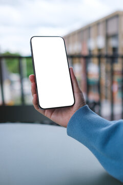 Vertical mockup image of a woman holding and using mobile phone with blank desktop screen in cafe