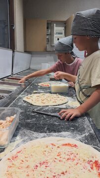 Children adding cheese toppings to pizzas in a kitchen