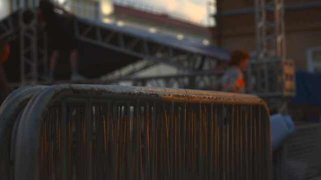 Weathered metal crowd control barrier with warm sunset highlights in backstage event setting, shallow depth of field and low viewpoint emphasizing textured rust and flaking paint on rounded top rail